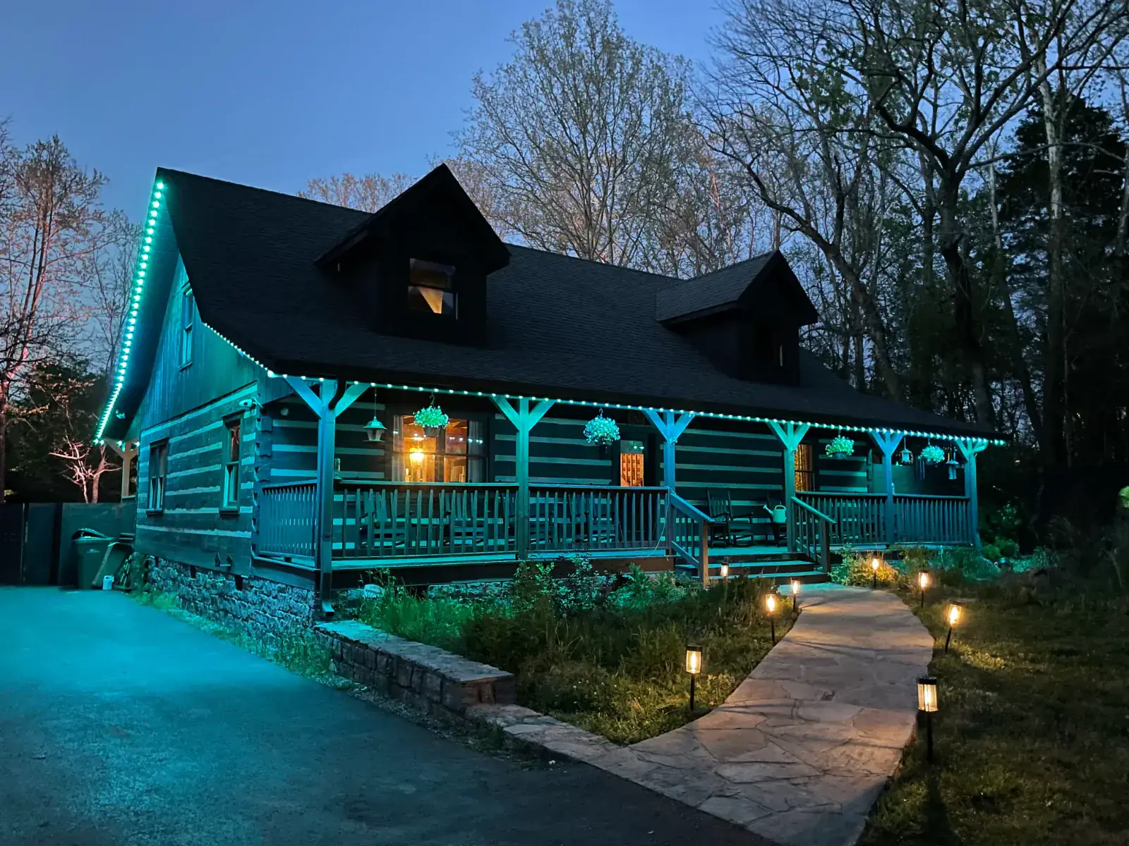 A log cabin with teal OMNI RGB programmable roofline lighting glowing along the eaves and porch at dusk