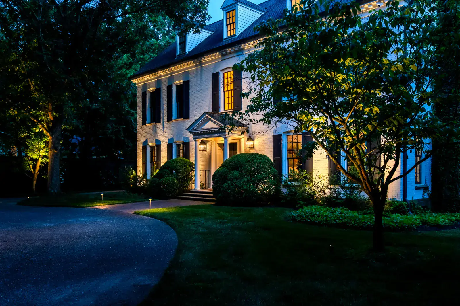 Full Georgian Colonial estate facade with warm LED up-lighting, cornice accent lighting, columned portico, and flanking tree uplighting at blue hour, Belle Meade, TN