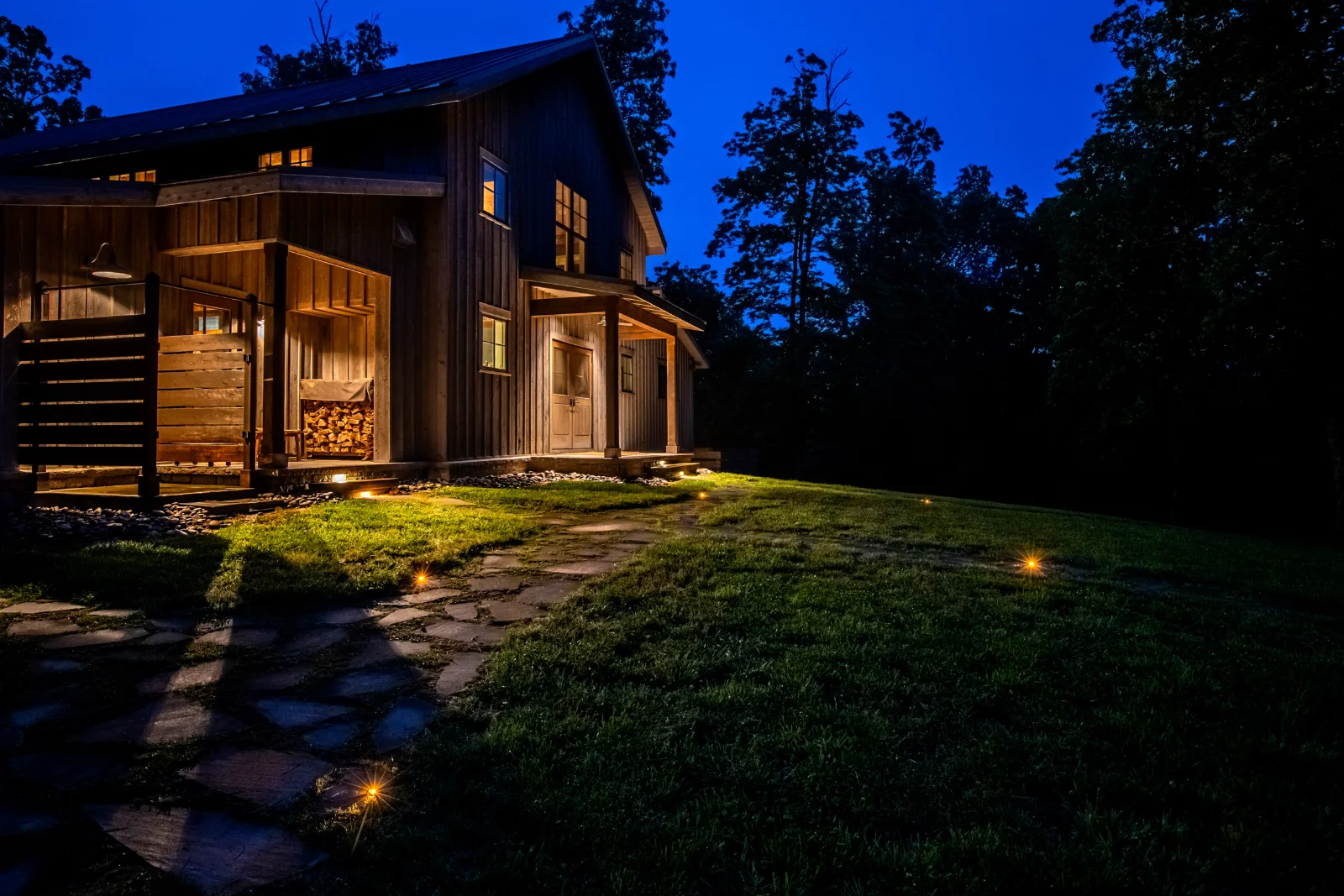 A rustic barn-style Middle Tennessee home illuminated at night with warm ground lights along a stone path
