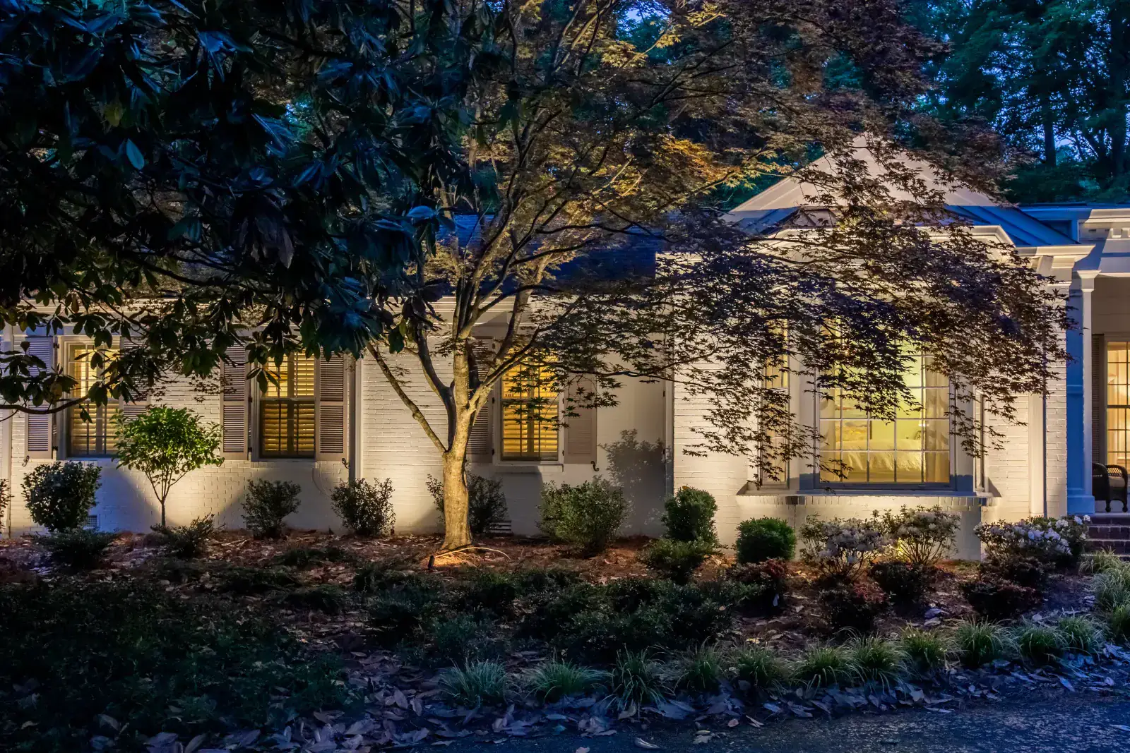 White-brick single-story estate with warm facade up-lighting and Japanese maple tree uplighting framing the front elevation at dusk, Belle Meade, TN