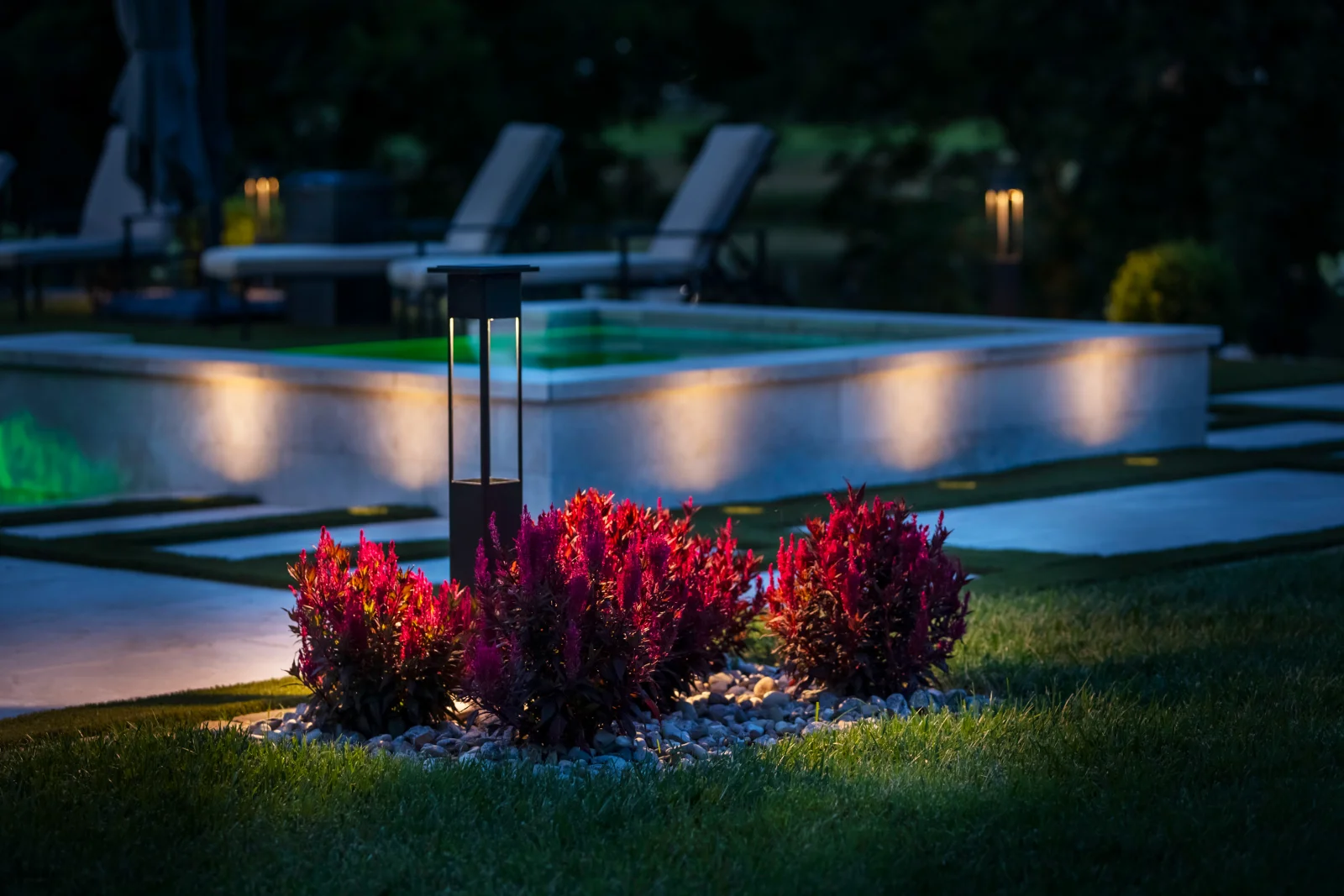 Outdoor lighting installation showing a bollard path light beside red flowering shrubs with pool surround lighting at night in Middle Tennessee by Light TN