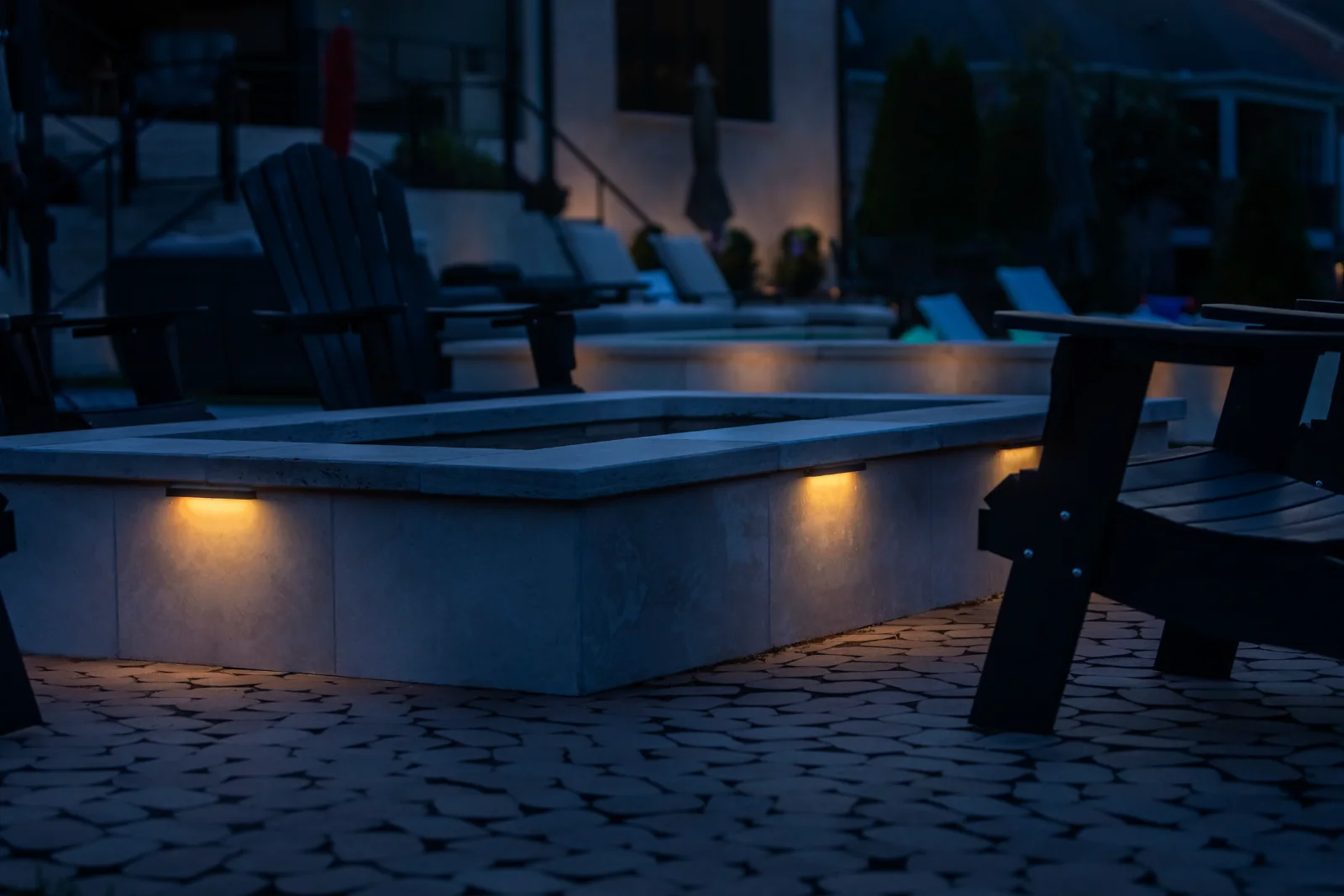 Warm step lights illuminating a stone patio and pool area at night, designed by Light TN