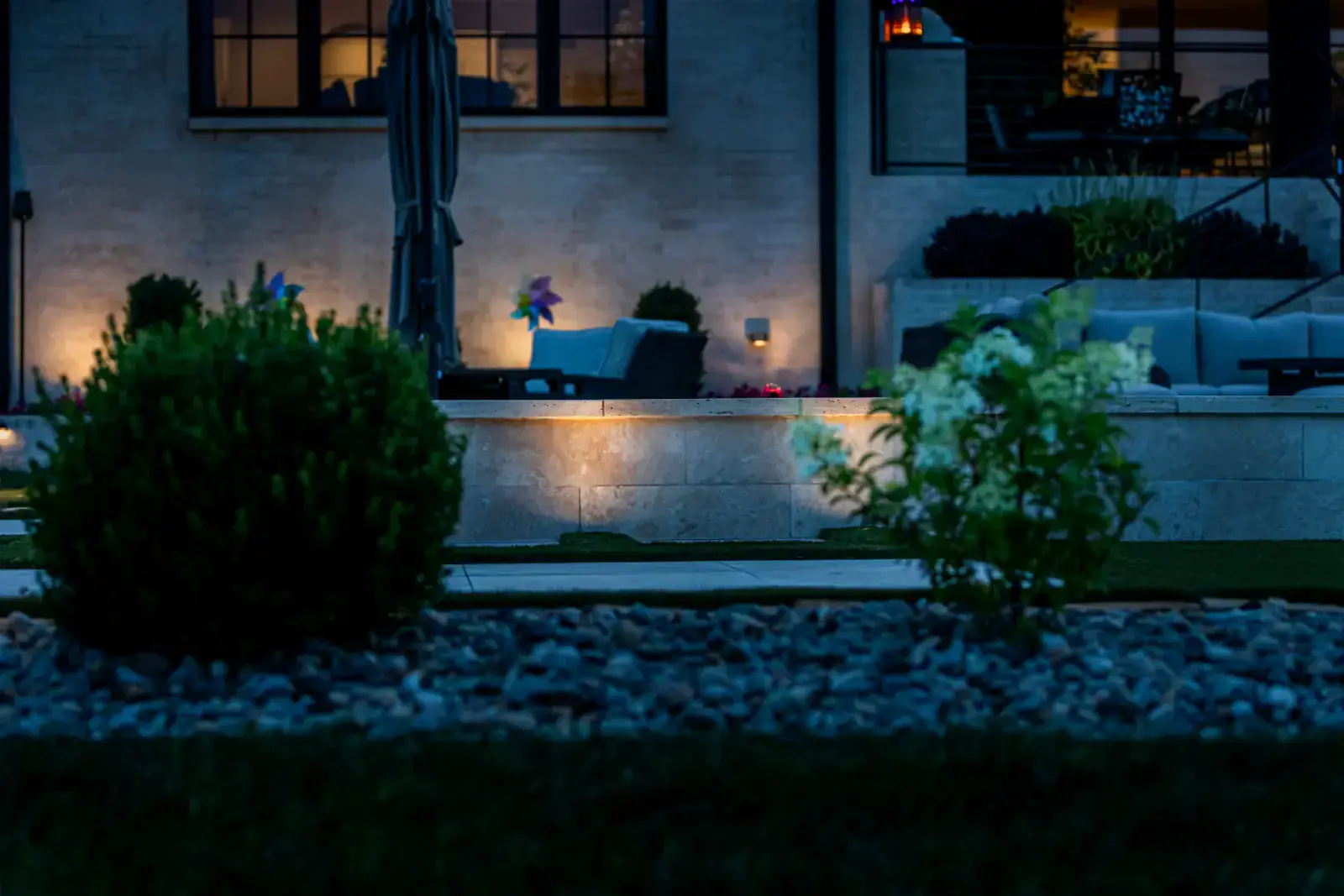 Warm LED step lights mounted in a limestone patio retaining wall illuminating a modern outdoor lounge area with pool and Adirondack chairs at dusk, Middle Tennessee