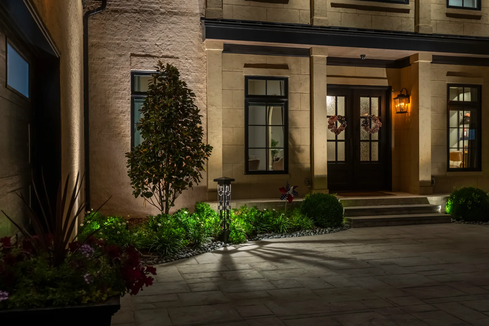 A Nolensville home facade and landscaping illuminated after dark, with bollard path light and warm uplighting on stone