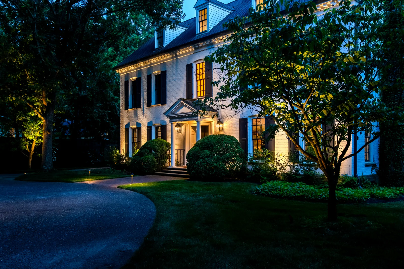 White-brick colonial estate with architectural uplighting, tree up-lighting, and roofline lighting at blue hour, Brentwood TN