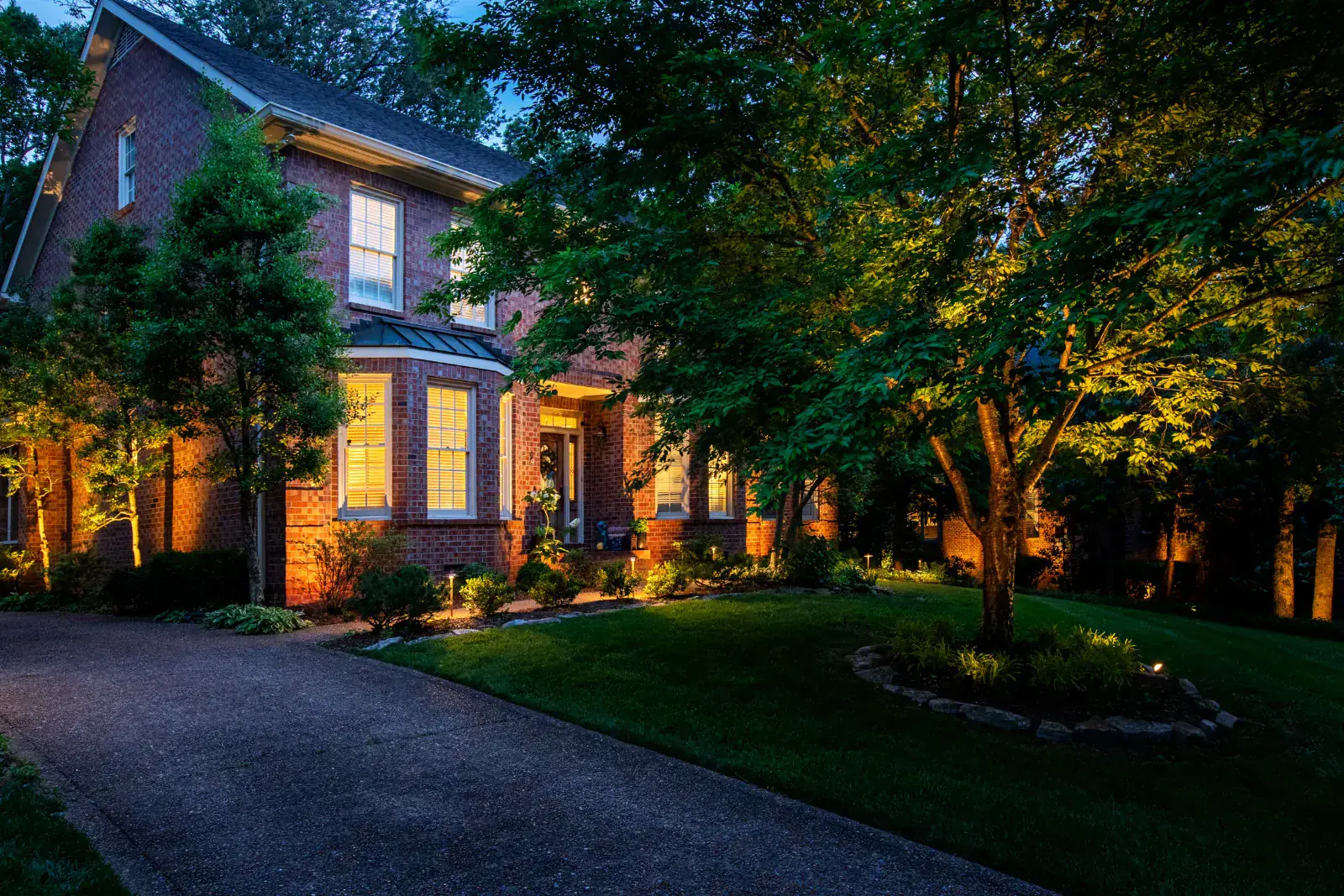Nashville brick home with landscape and tree up-lighting at blue hour, warm uplights framing mature canopy