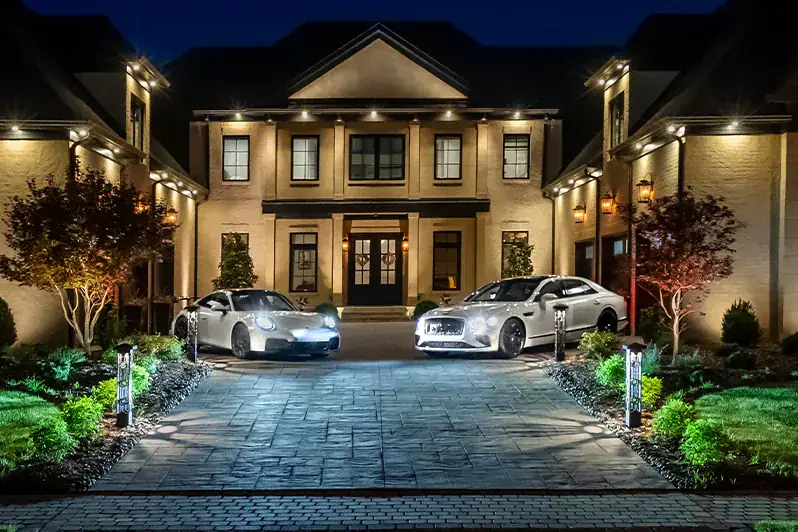 A Belle Meade estate fully illuminated at night with architectural uplighting, landscape lighting, and luxury cars in the foreground