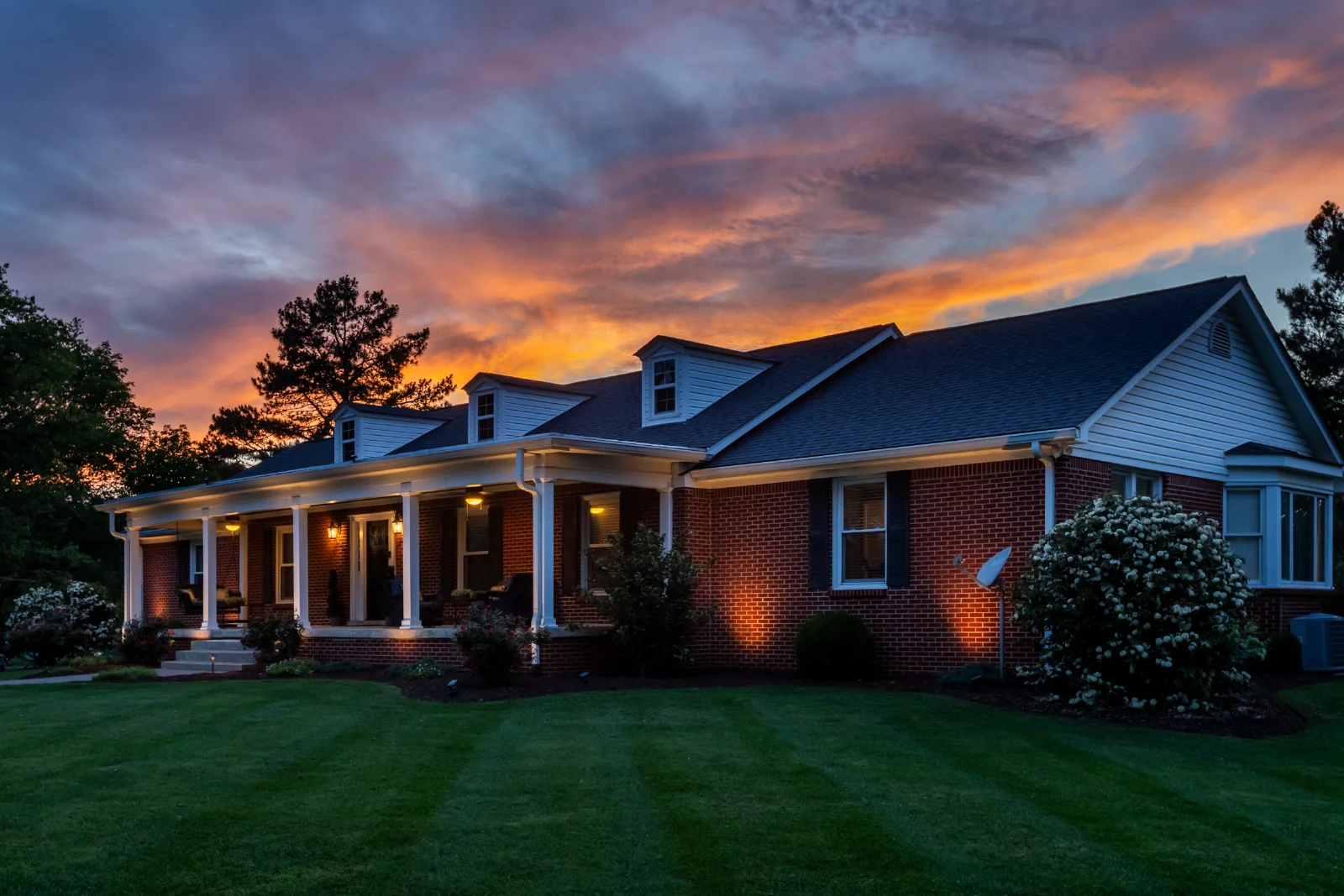 A brick Mount Juliet home with architectural lighting glowing at sunset, warm uplighting on the facade and porch
