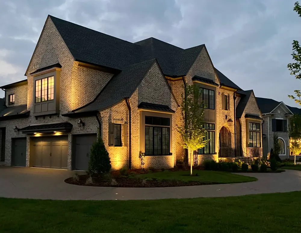 A Nashville estate lit at dusk with warm uplighting on brick facade and landscaped trees